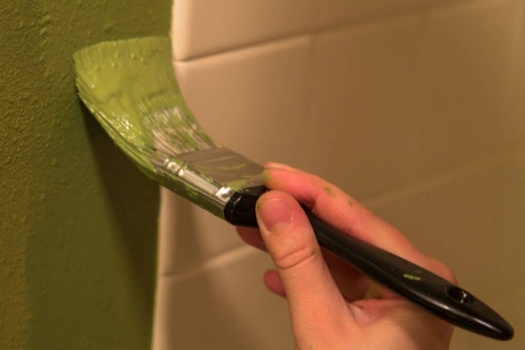 A woman brushing the bathroom wall with main green paint