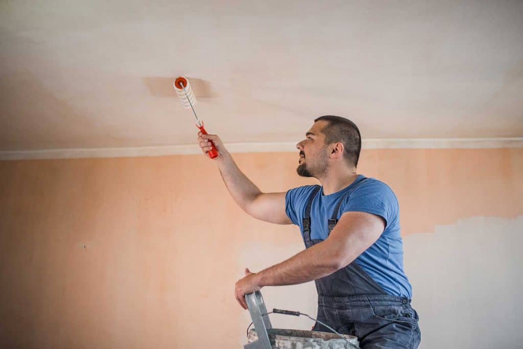 Painter standing on a ladder painting the ceiling with paint roller