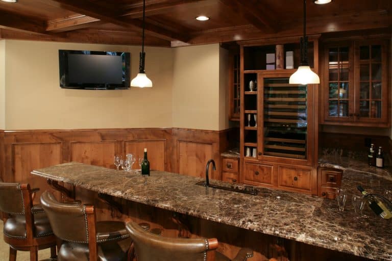Rustic interior of a basement with wooden cabinets, marble bar countertop, and hardwood ceiling, Should I Put A Bar In My Basement?