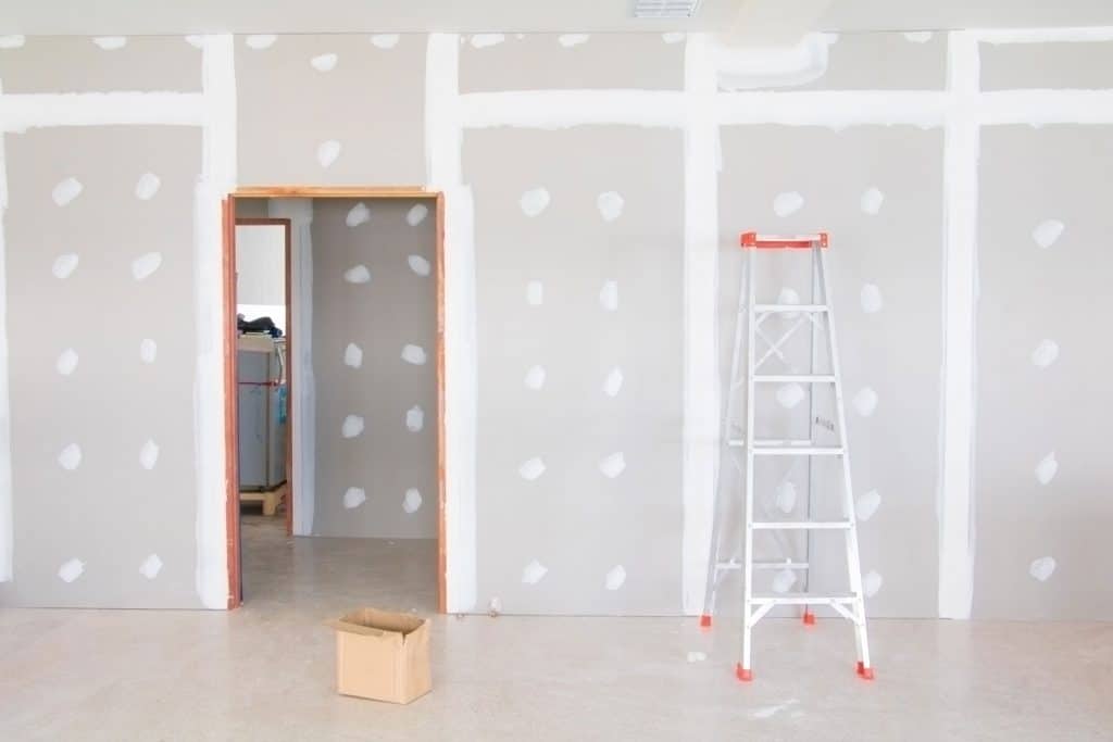 A basement with plastering on the drywall with a ladder and boxes filled with equipment