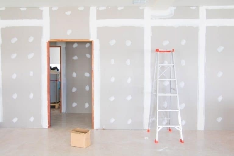 A basement with plastering on the drywall with a ladder and boxes filled with equipment, Should You Drywall A Basement Ceiling?