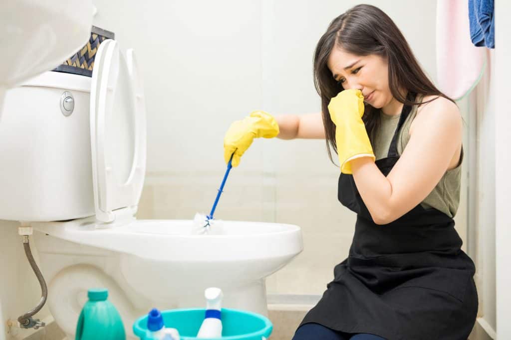 A woman covering her nose while cleaning the toilet