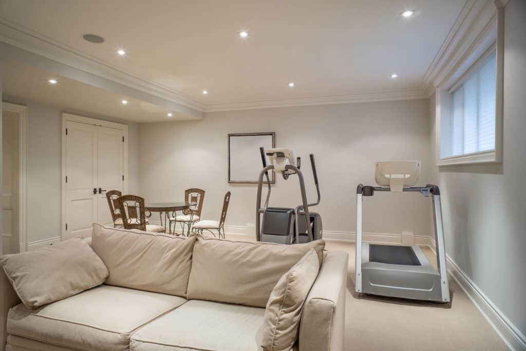 Interior of a beige colored basement with recessed lighting and gym equipments
