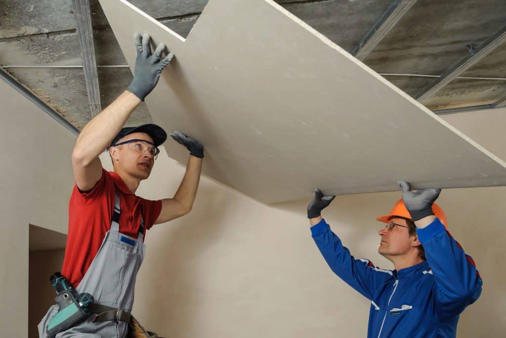 Two workers installing a gypsum board on the ceiling