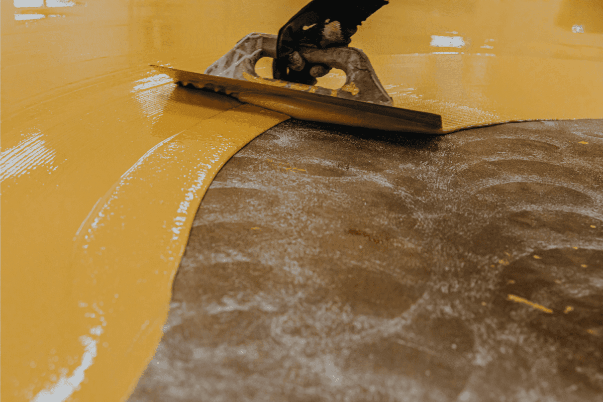 Worker, coating floor with self-leveling epoxy resin in industrial workshop