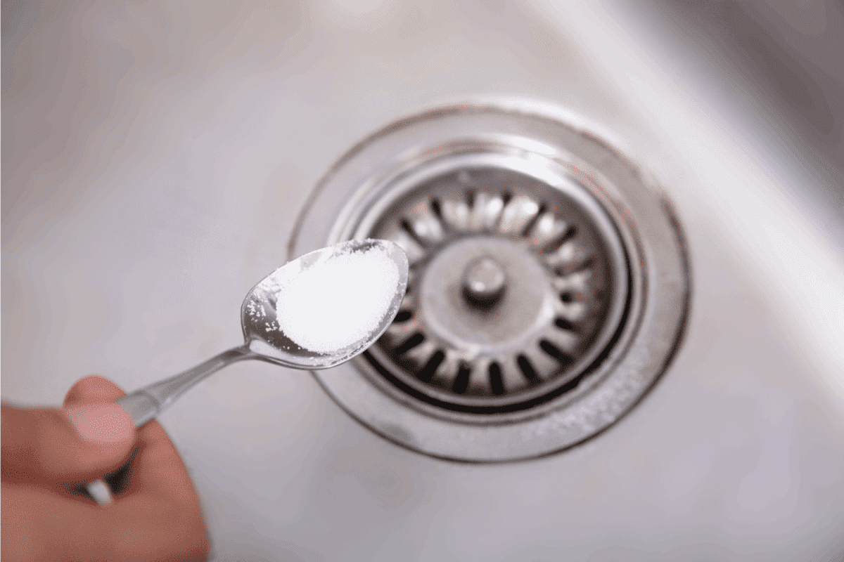 A Person Putting The Baking Soda With Spoon On Drain