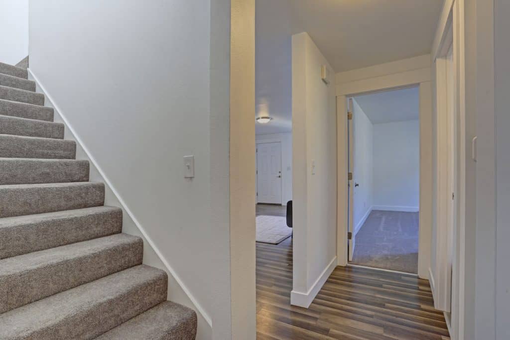 A gorgeous and nicely lit basement with wooden flooring, carpeted stairs, and white painted walls, Does A Basement Door Have To Be Fire Rated?