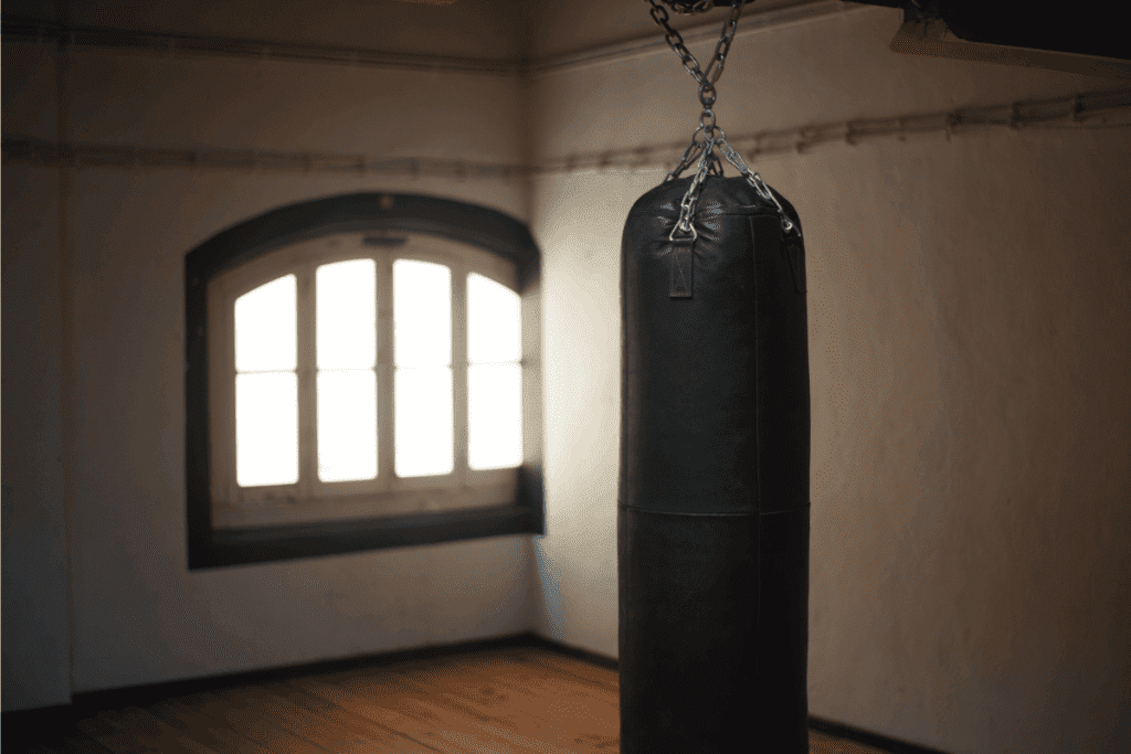 Boxing gym. Hanging black sandbag in front of closed window. How To Hang A Heavy Punching Bag In Basement