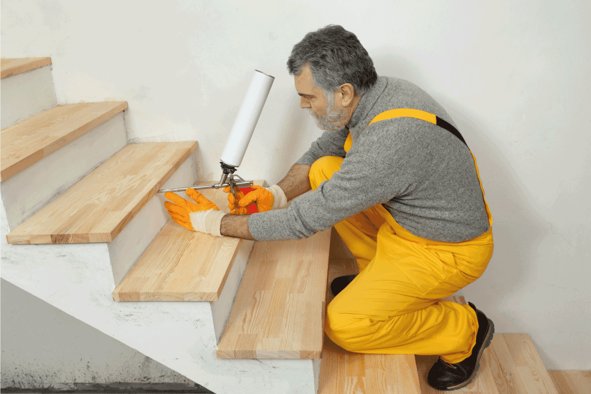 Construction worker fixing wooden stairs with polyurethane spray gun