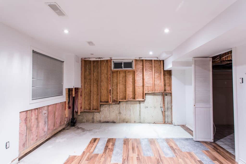 Interior of a modern and unfinished basement with wooden walls, opened wooden framing, and recessed lighting, How To Heat An Unfinished Basement
