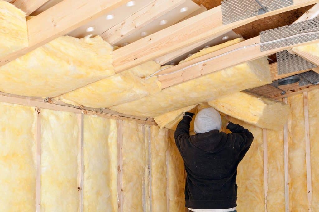 Worker installing fiberglass batt insulation between roof trusses