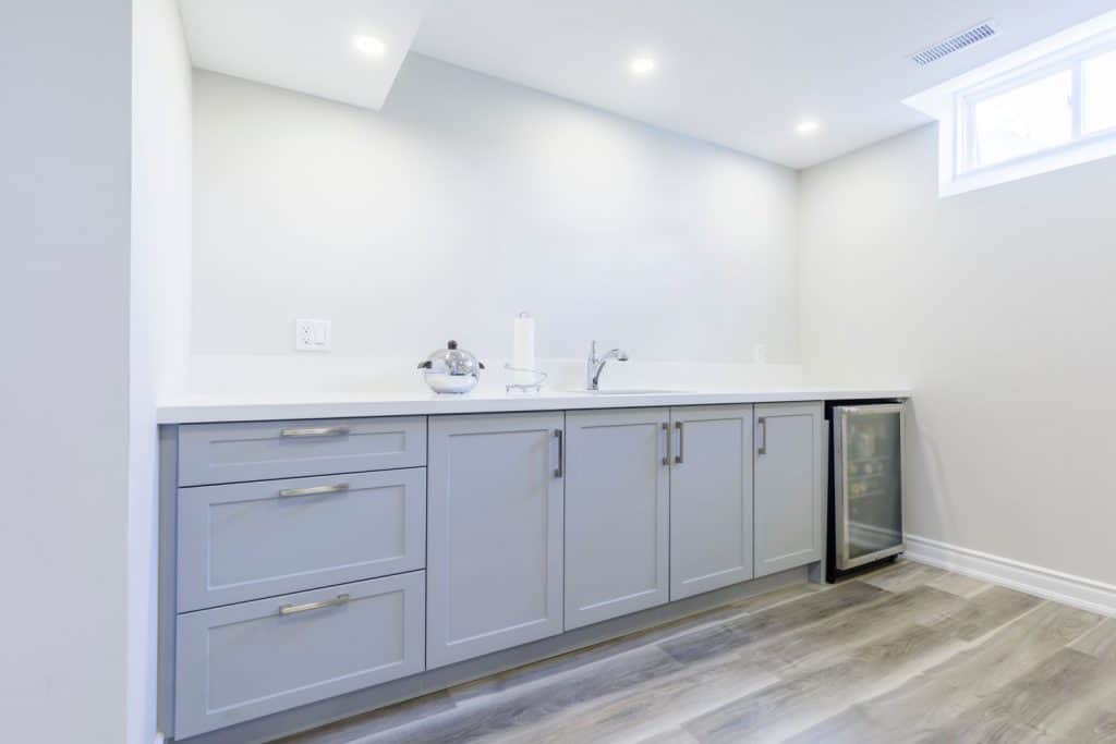 A basement sink with gray cabinets with white painted walls and recessed lighting