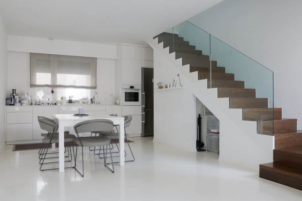 A gorgeous and modern kitchen with white epoxy flooring and wooden stairs with glass walls