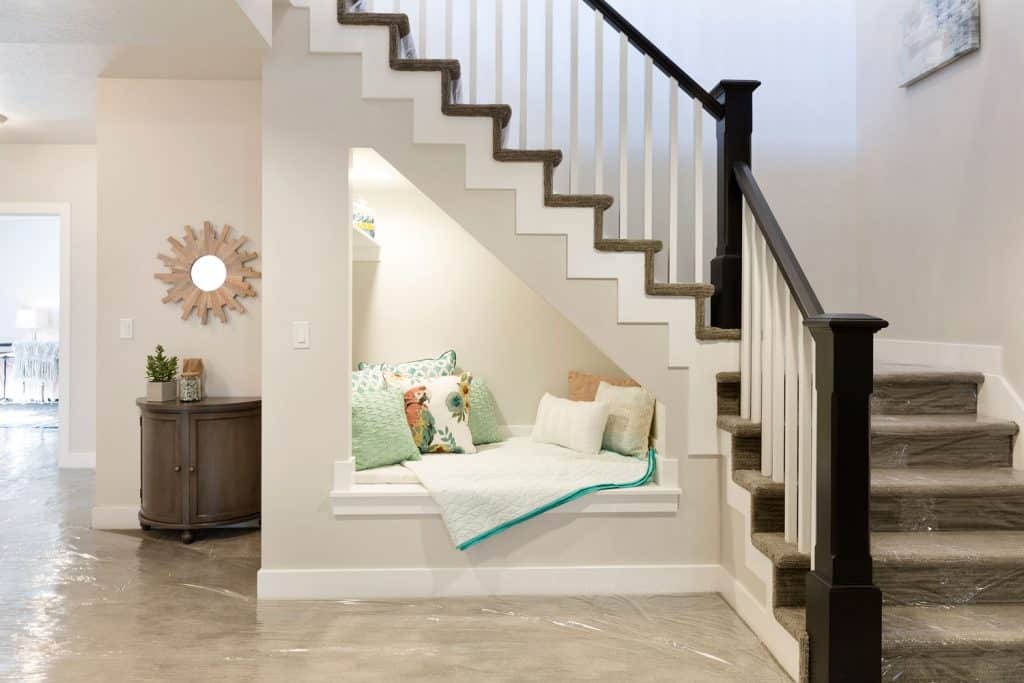 A green carpeted basement stair with white painted wall with a small resting area underneath the stairs