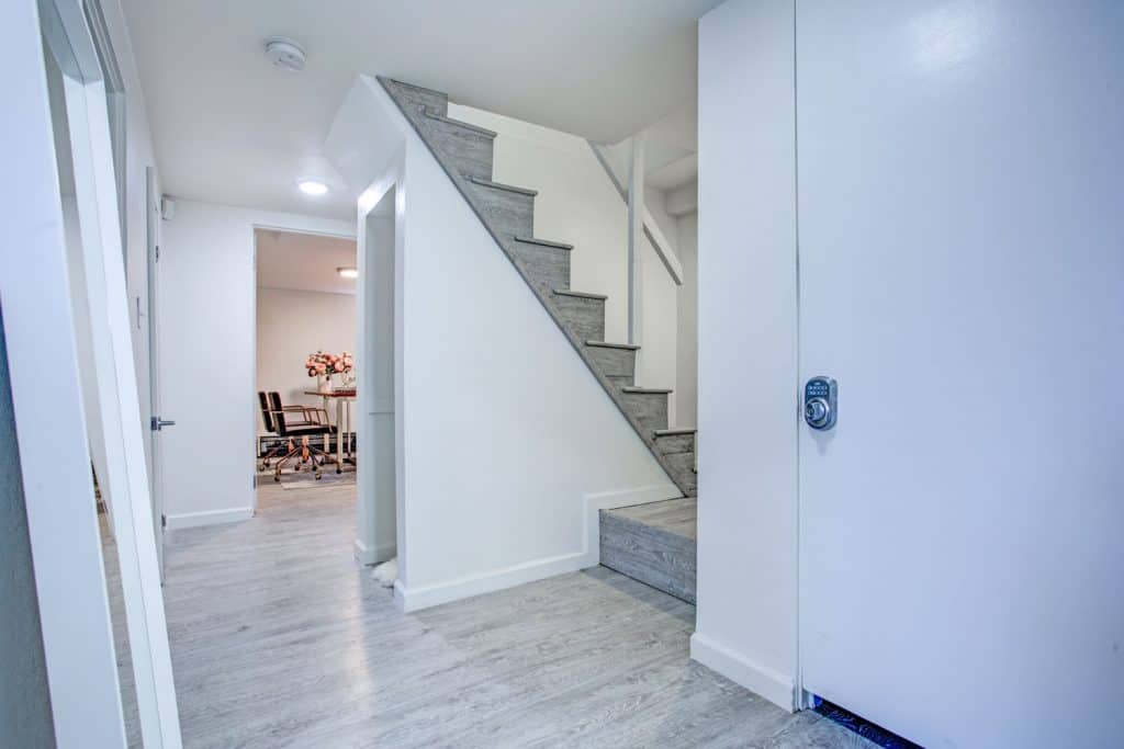A spacious basement with laminated vinyl flooring, carpet staircase and white walls