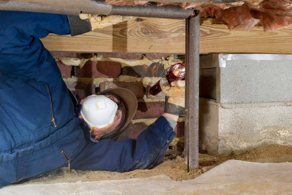 A worker checking the pipes under the crawl space of the basement