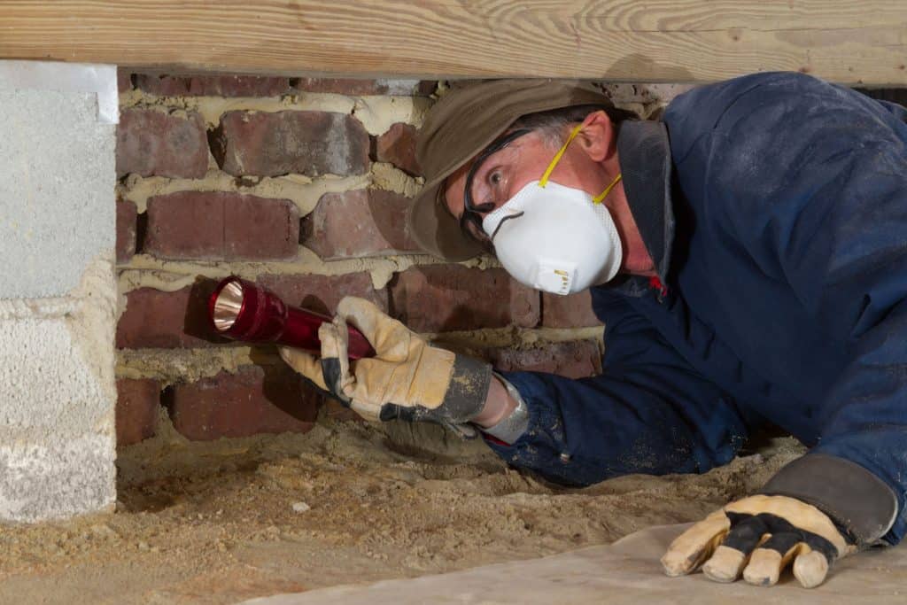 A worker going under the crawl space checking the pipes