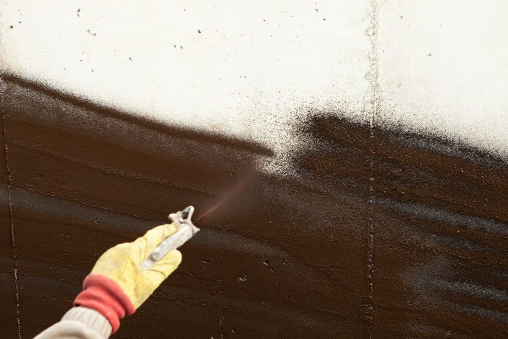 A worker spraying waterproof foam in the basement exterior wall