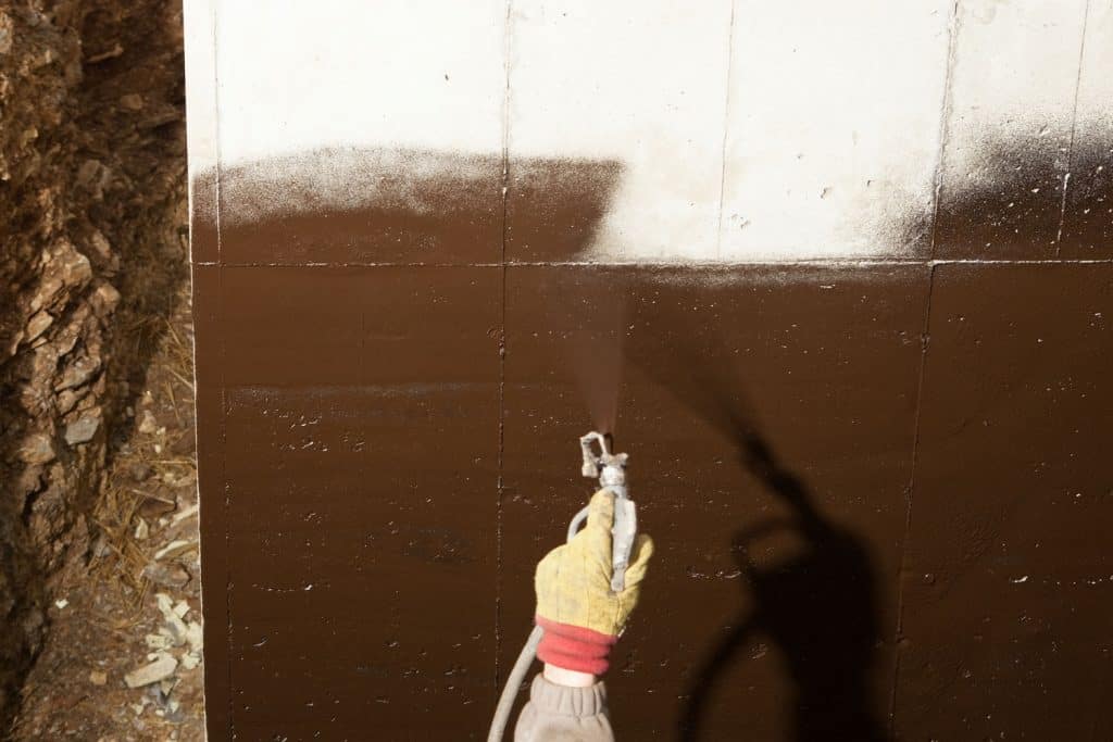 A worker spraying waterproof insulation on the basement exterior wall