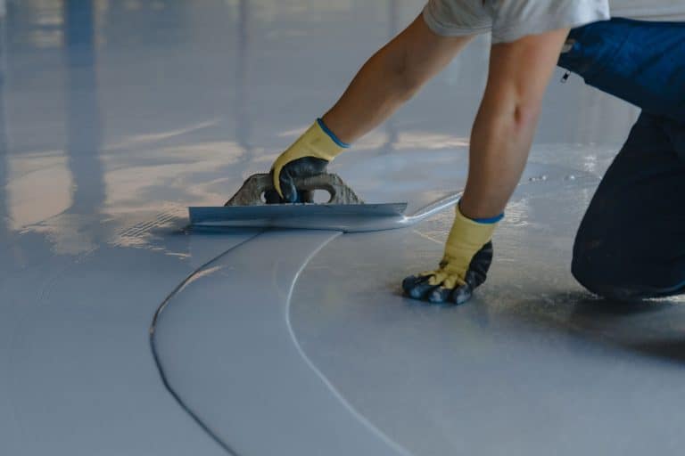 A worker using a trowel in spreading gray epoxy coating, Pros & Cons Of Epoxy Floor Coating