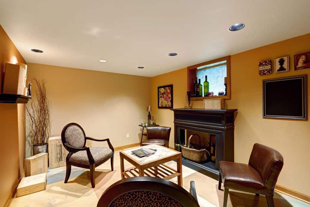 Cozy sitting area in basement room with decorative fireplace, chairs and small wooden table