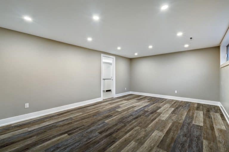 Empty interior of a living room with wooden vinyl tiled flooring, gray walls and recessed lighting, Does A Basement Floor Drain Need A Trap?