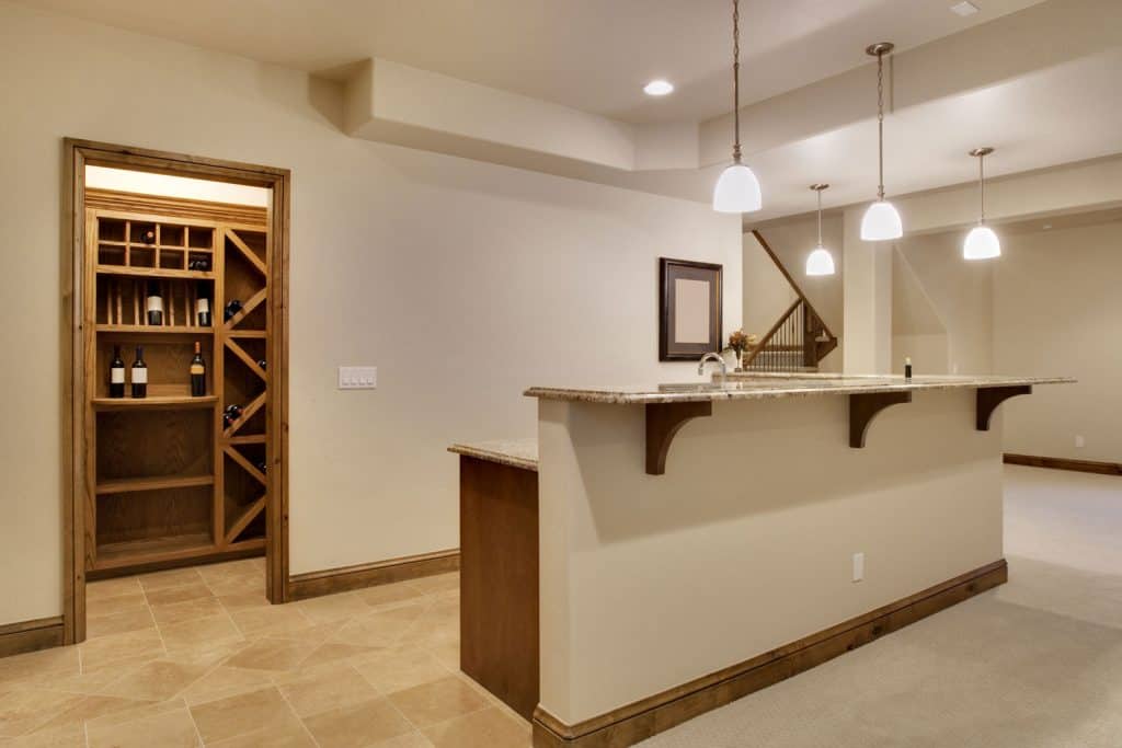 Interior of a cream painted basement walls, wooden cabinets in the breakfast bar and dangling lamps