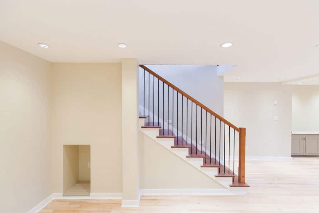 Interior of a modern and neatly painted white wall basement with a wooden floor staircase