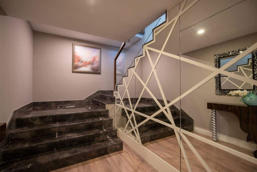 Interior of a modern basement with wooden flooring, marble tiles in the stairs and a huge mirror under the stair case