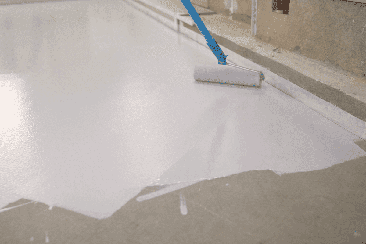 Manual painting of a white floor with a paint roller for waterproofing. A worker paints the concrete floor with white paint