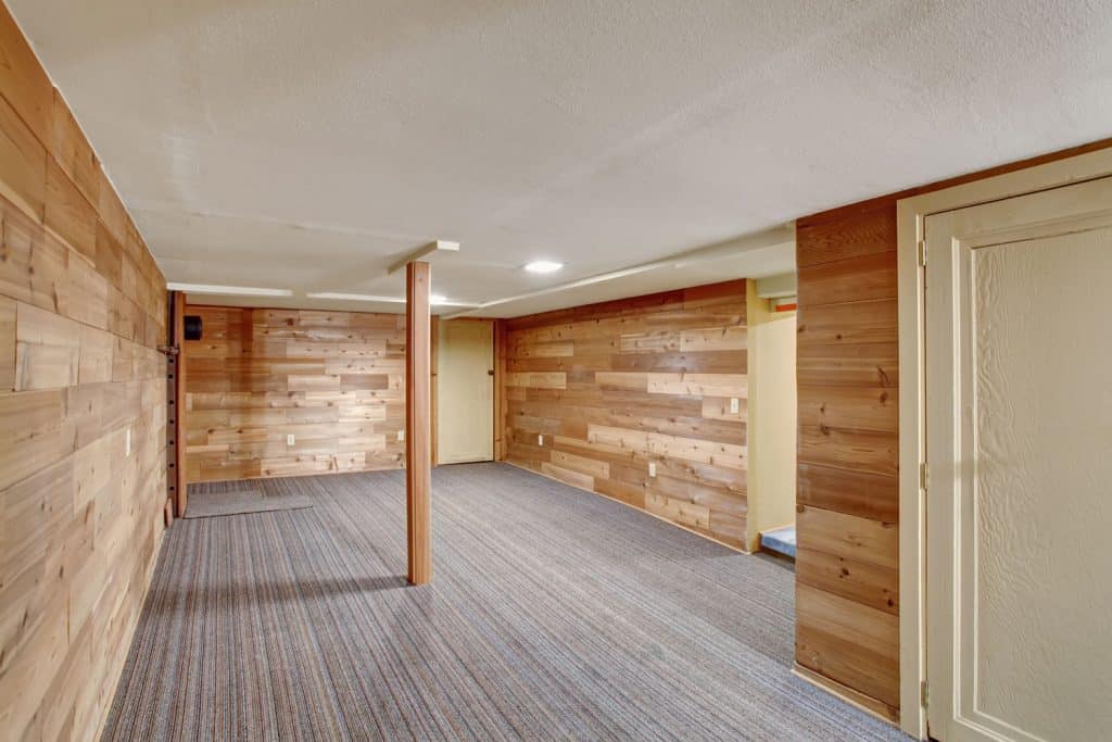 Modern rustic inspired basement with wooden plank cladding carpeted flooring and a post in the middle