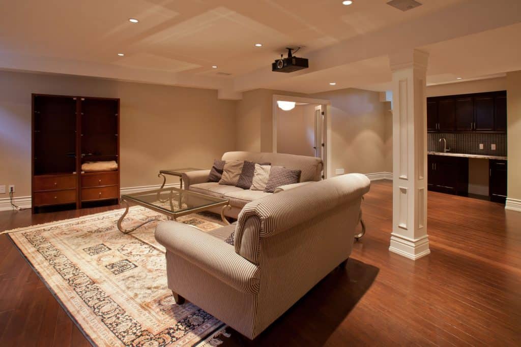 Rustic inspired basement with wooden flooring, striped sofas with beige colored walls and recessed lighting