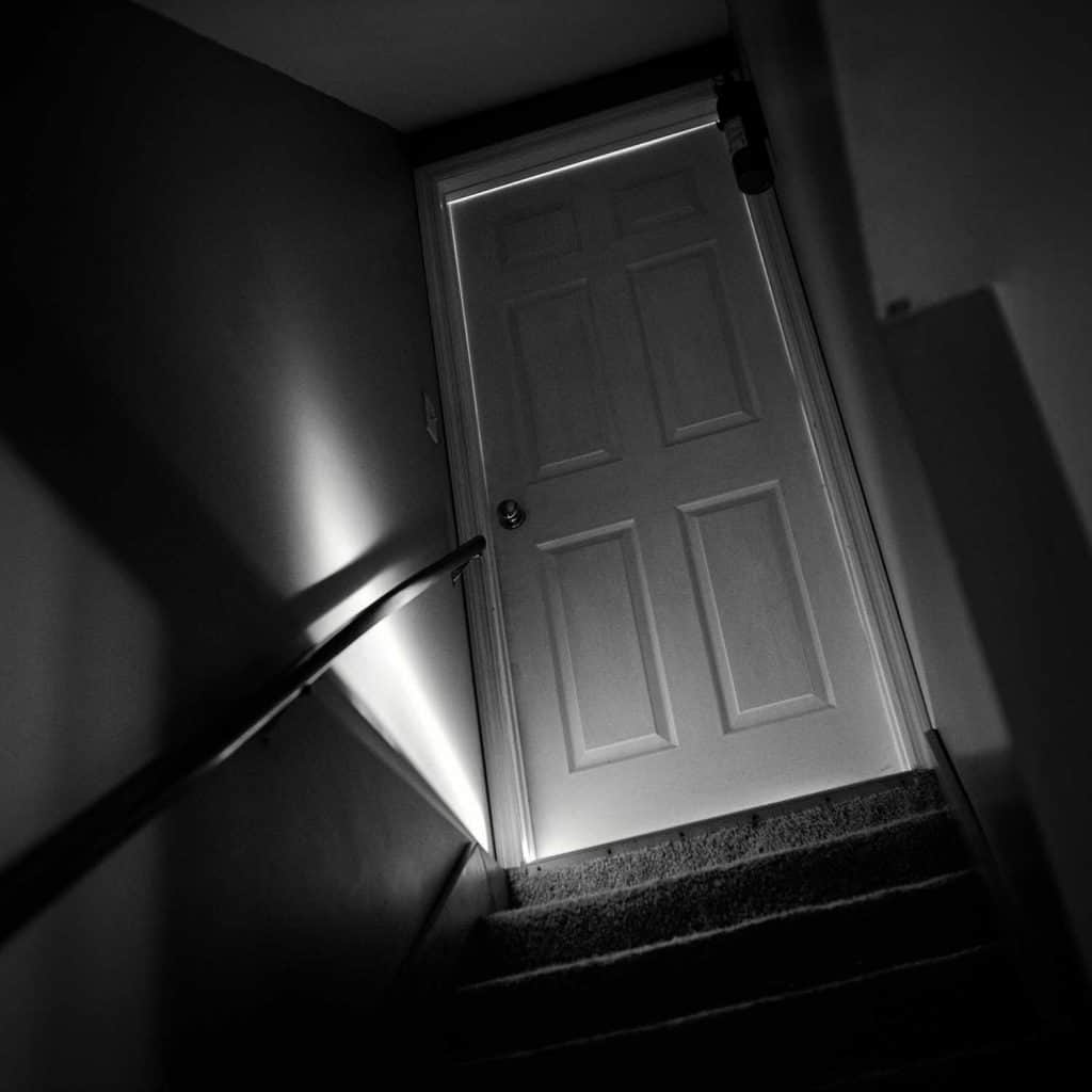 Shot of a basement door in the dark with bright sunlight bursting through the bottom