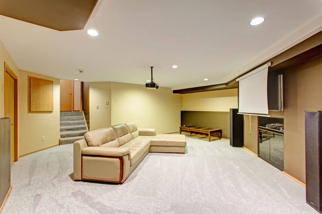 Spacious and modern carpeted basement flooring with tan walls and white ceilings