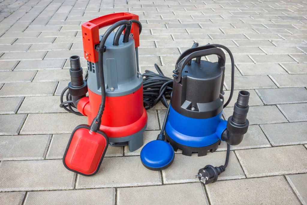 Two household submersible pump with plastic housings on stone floor of courtyard

