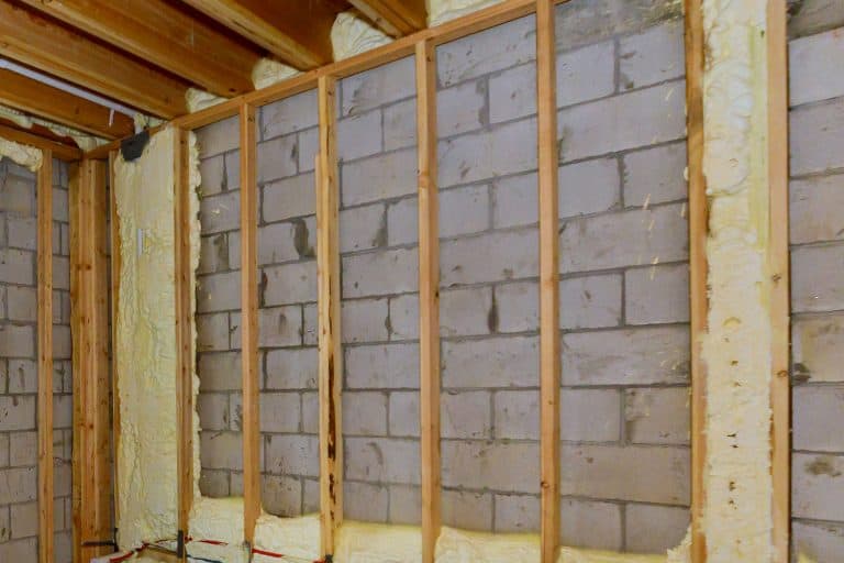 Wooden framing of a basement with unfinished insulation and the floor joist above, How To Frame A Basement Wall Parallel To Floor Joists