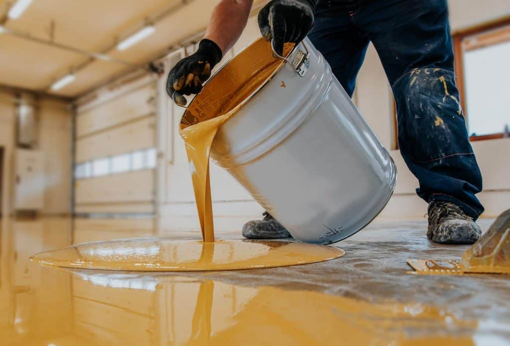 Worker applying a yellow epoxy resin bucket on floor for the final coat
