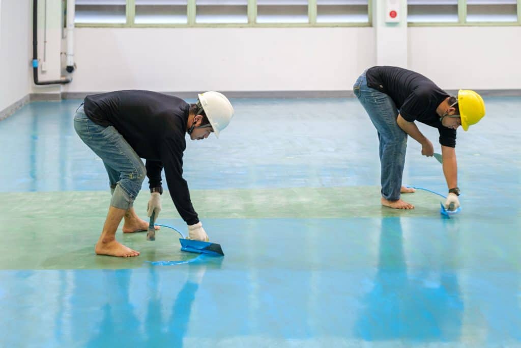 Workers spreading blue epoxy in the stadium flooring