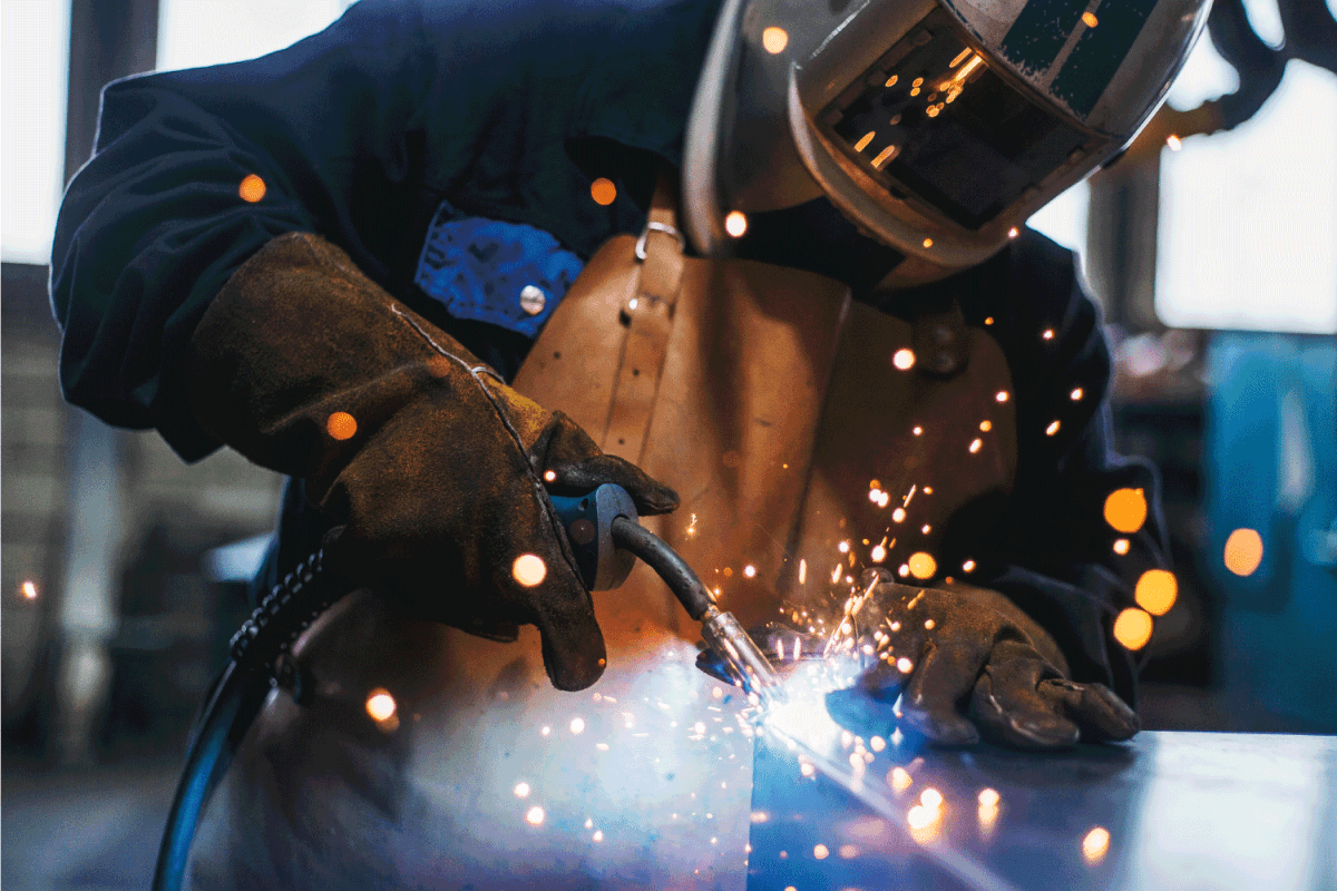 welder wearing complete safety equipment welding metals on workbench