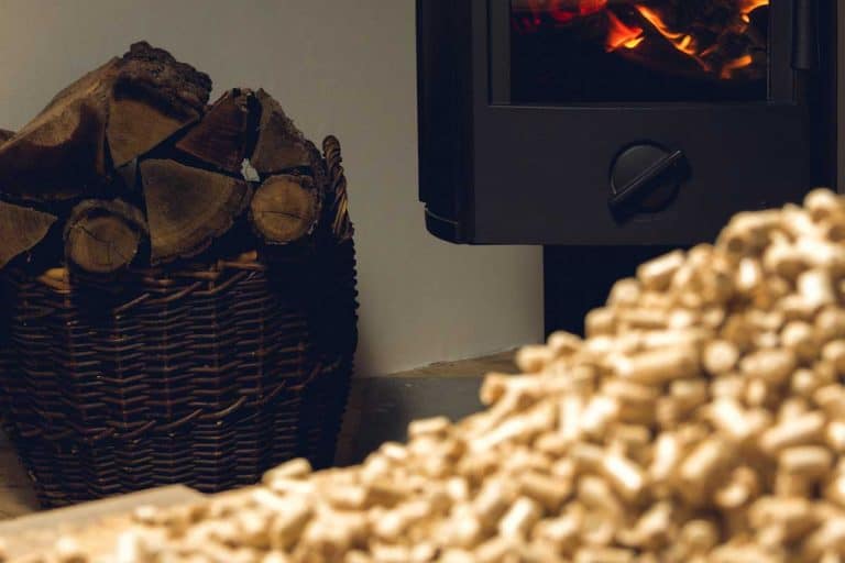 Wooden pellets lie on a table in front of a fireplace with burning firewood, Can You Vent A Pellet Stove Through A Basement Window?