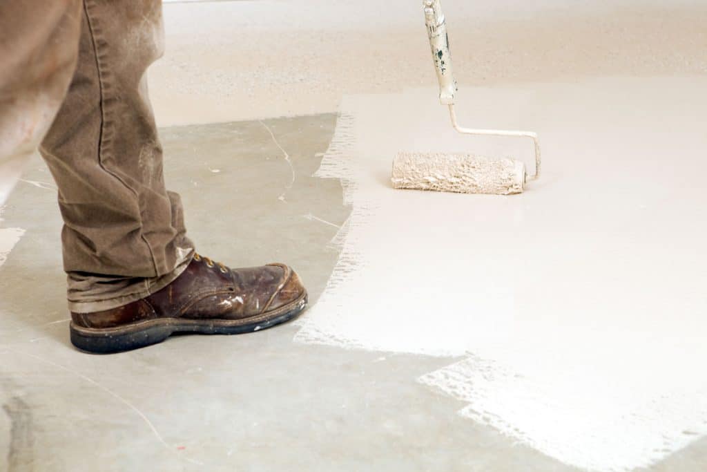 Worker applying epoxy paint on the basement floor