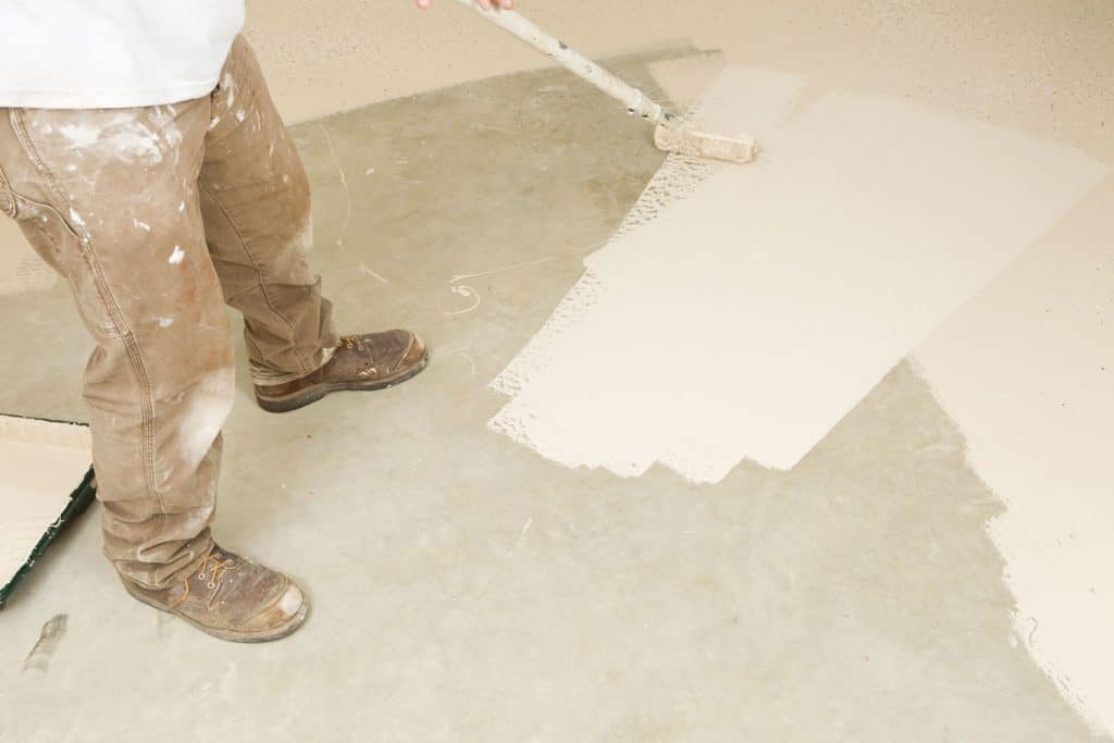 Worker spreading white epoxy paint on the basement floor