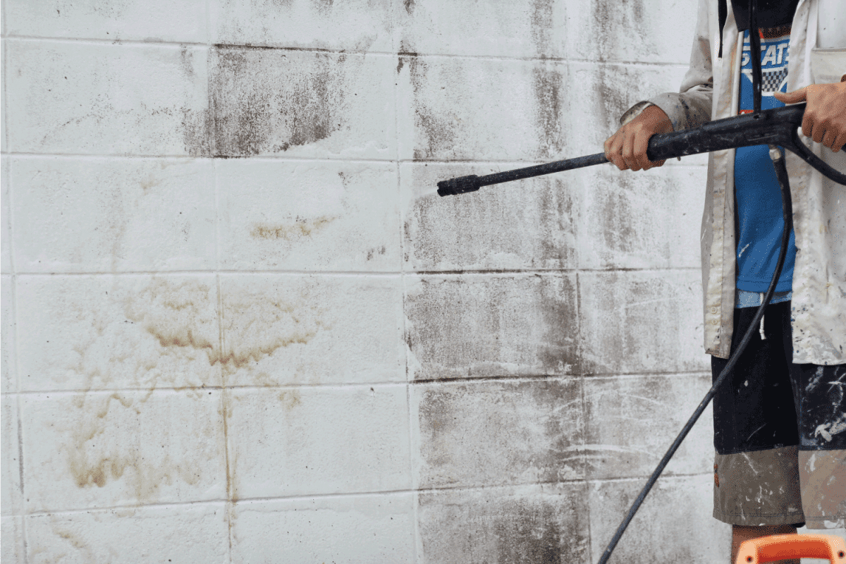 a man wearing hat and white shirt using high pressure cleaners to clean dirty wall