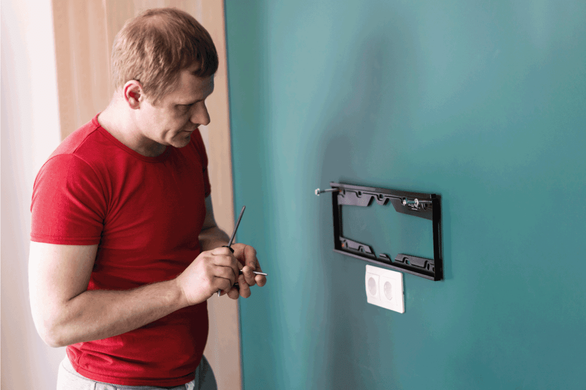 repair and decoration service. a man attaches a TV mount to a wall