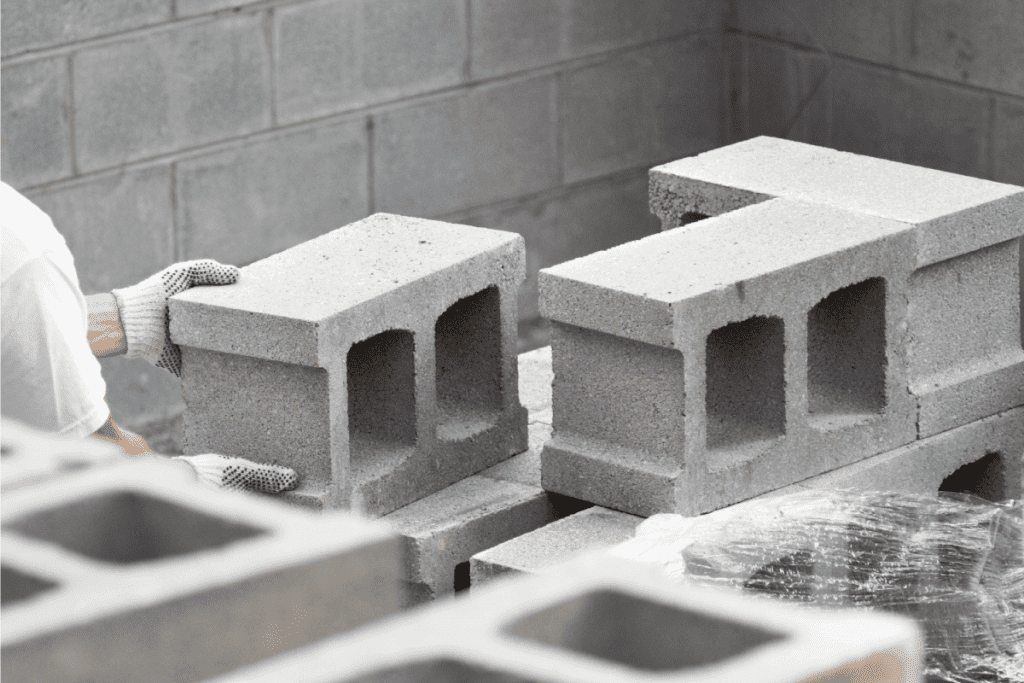 A worker wearing non-slip safety gloves is stacking concrete building blocks in a new residential basement foundation. How To Clean Cinder Block Basement Walls [Plus Mold & Stain Removal]